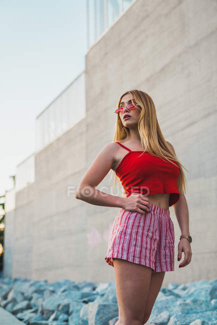 Стильна молода жінка в шортах і червоний бак зверху на бетонну стіну — стокове фото