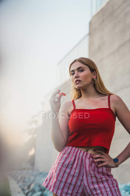 Blonde young woman in shorts and tank top holding sunglasses outdoors — Stock Photo