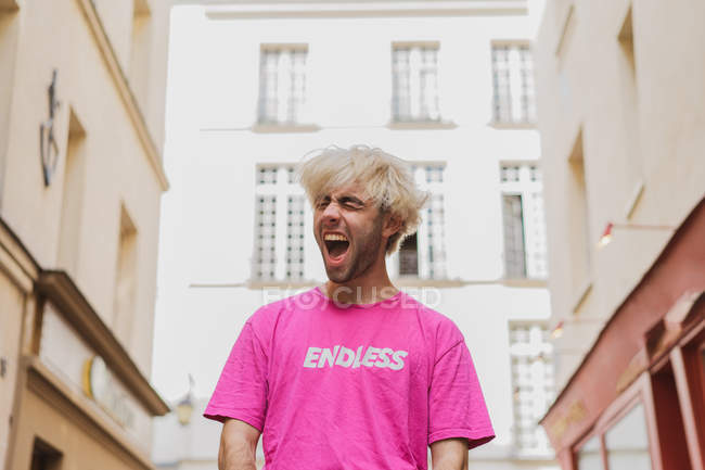 Homme élégant aux cheveux blonds et t-shirt rose criant dans la rue — Photo de stock