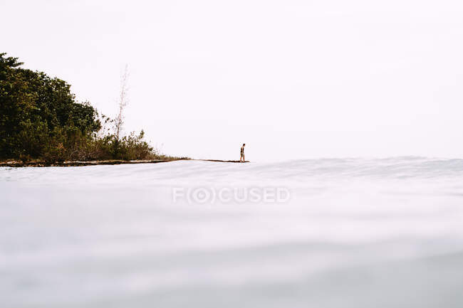 Anonyme Person, die auf einem Kap inmitten des blauen klaren Wassers des Ozeans und der grünen Küste Kubas steht. — Stockfoto