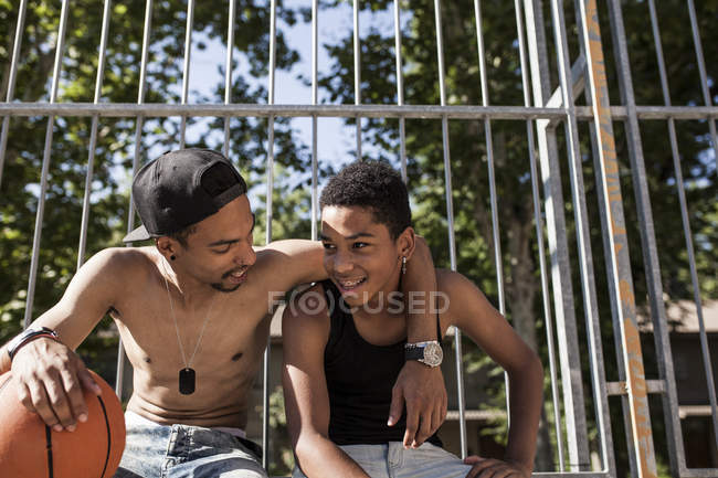 Afro young brothers sitting with basketball on court outdoors and embracing — Stock Photo