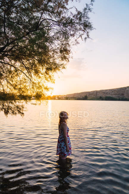 Чувственная женщина в летнем платье, стоящая на озере на закате — стоковое фото