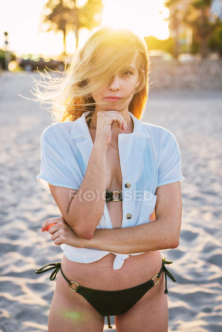 Wunderschöne Frau, die bei Sonnenuntergang am Strand steht und in die Kamera schaut — Stockfoto