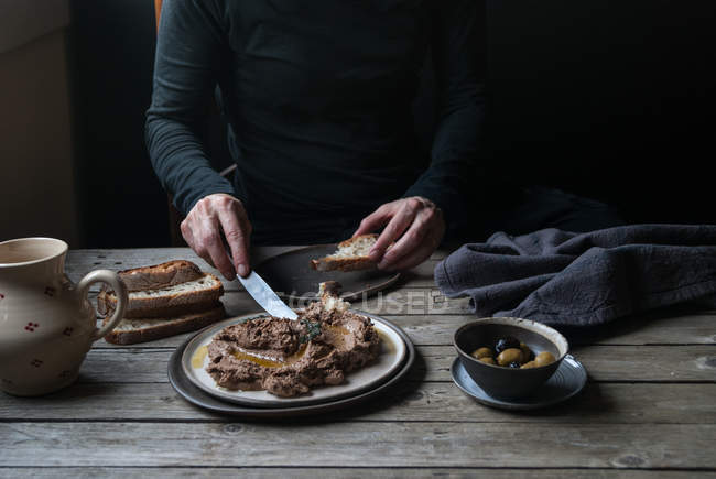 Male hands spreading lentil pate on bread on rustic wooden table — Stock Photo