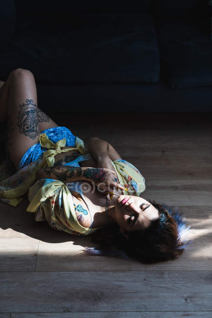 Sensual tattooed woman lying with eyes closed on floor — Stock Photo
