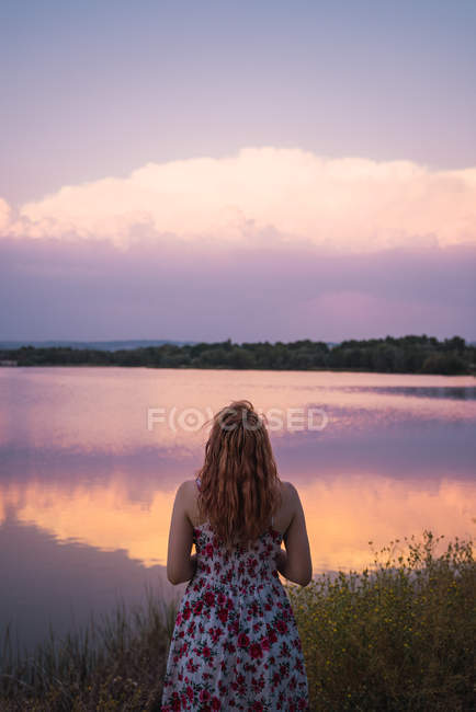 Frau im Sommerkleid steht bei Sonnenuntergang am Seeufer — Stockfoto