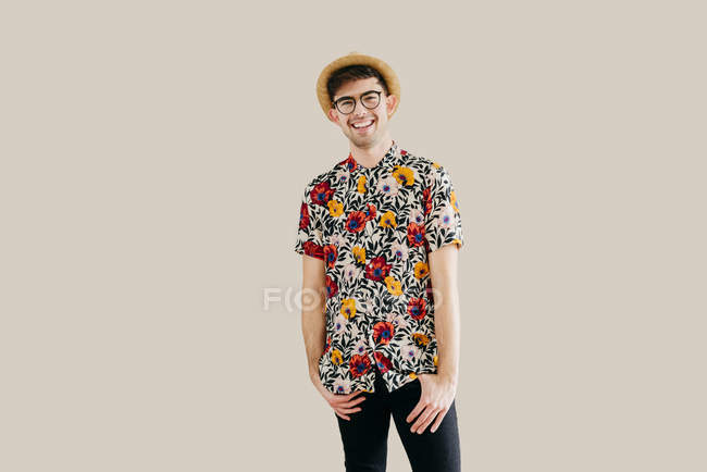 Stilvoller junger Mann mit Strohhut und gemustertem Hemd posiert vor grauer Wand — Stockfoto
