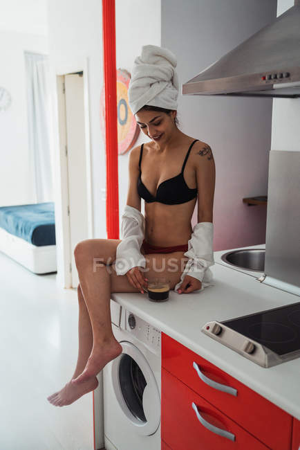 Mulher sensual em lingerie com toalha no cabelo sentado no balcão com xícara de café — Fotografia de Stock