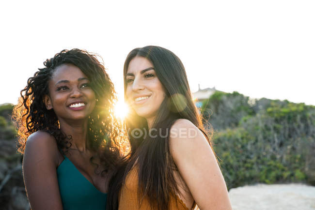 Diversas mujeres jóvenes de pie y sonriendo en el fondo de la naturaleza en retroiluminación - foto de stock