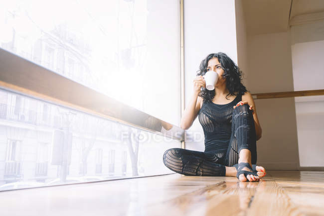 Frau trinkt Kaffee, während sie im Tanzkurs auf dem Boden sitzt — Stockfoto