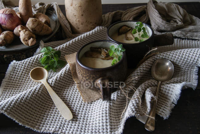 Cuencos de sabrosa sopa de alcachofa de Jerusalén con ingredientes en la mesa de madera rústica - foto de stock