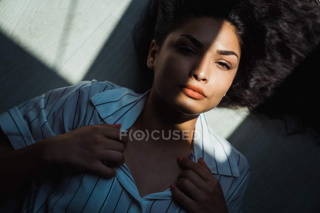 Young pensive brunette woman with long hair lying on floor in shadow and sunlight — Stock Photo
