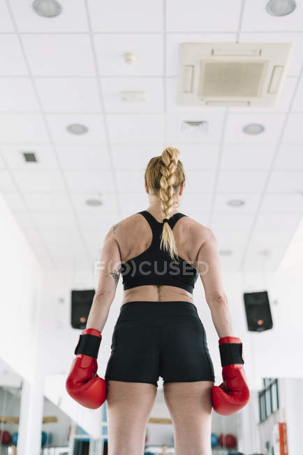 Вид сзади на мускулистую женщину в красных боксёрских перчатках, стоящую в спортзале — стоковое фото