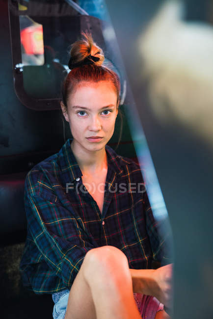 Mujer bastante joven en traje casual sentado dentro de la máquina de videojuegos y mirando a la cámara - foto de stock