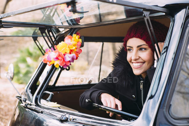 Улыбающаяся молодая женщина в теплой одежде сидит в машине и смотрит в сторону — стоковое фото