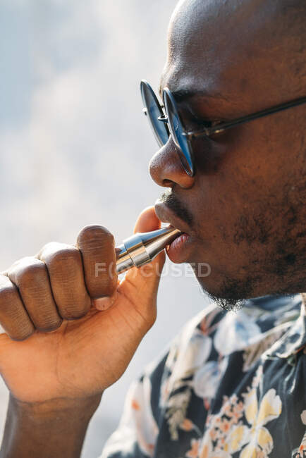 Schwarzer Mann mit Sonnenbrille. Er dampft draußen mit einer elektronischen Zigarre — Stockfoto