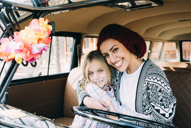 Abrazar a la mujer joven y chica rubia sentada en el coche viejo - foto de stock