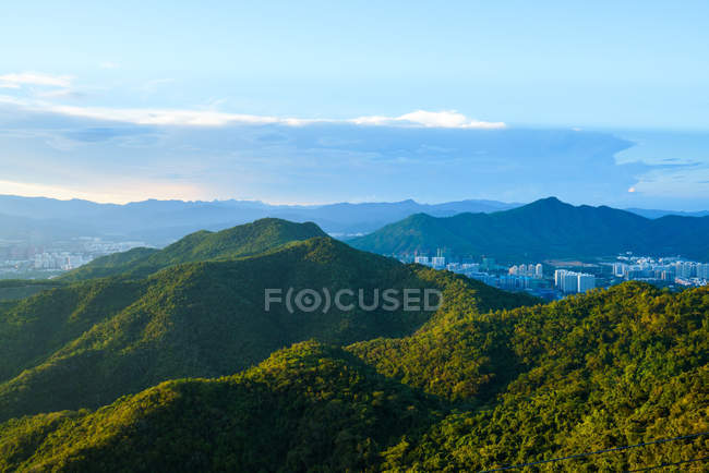 Landschaft üppiger tropischer Vegetation der Berge mit Stadt im Hintergrund im Tiefland, Phönixpark, Sanya, China — Stockfoto
