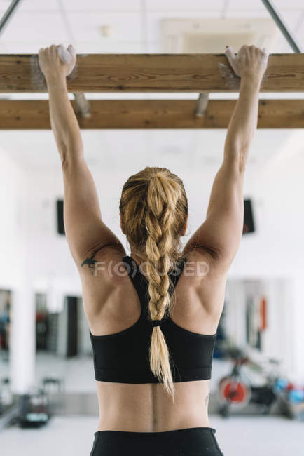 Задний вид сильной женщины в спортивной одежде висит на деревянной доске в тренажерном зале и тянет вверх — стоковое фото