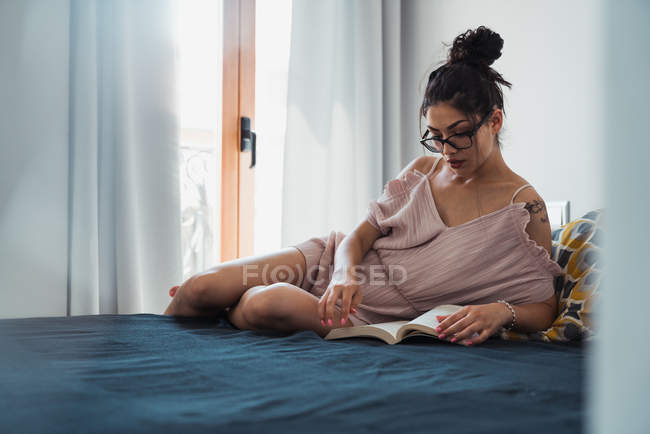 Fokussierte brünette Frau liest Buch auf dem Bett — Stockfoto