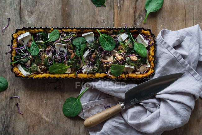Baked tart with polenta and spinach topped with pieces of crottin cheese in baking dish on wooden table — Stock Photo