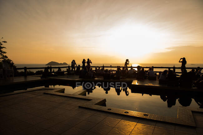 Silhouettes de personnes prenant des photos avec des smartphones au bord de la mer dans les lumières du coucher du soleil en Thaïlande. — Photo de stock