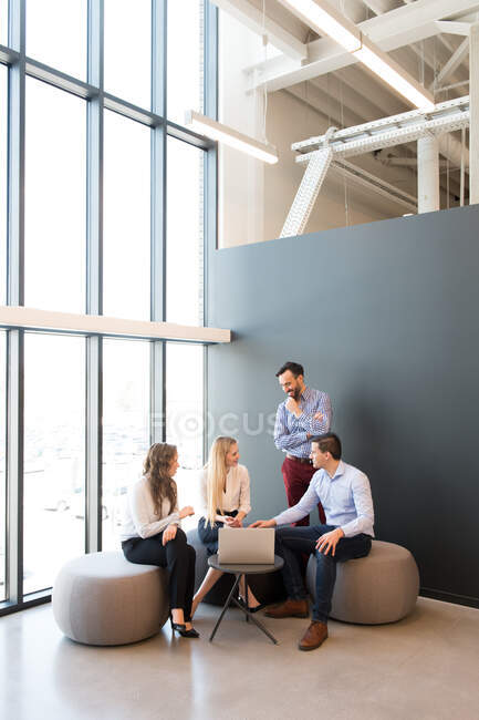 Stylish women and men sitting together around laptop on small table and talking while having meeting — Stock Photo