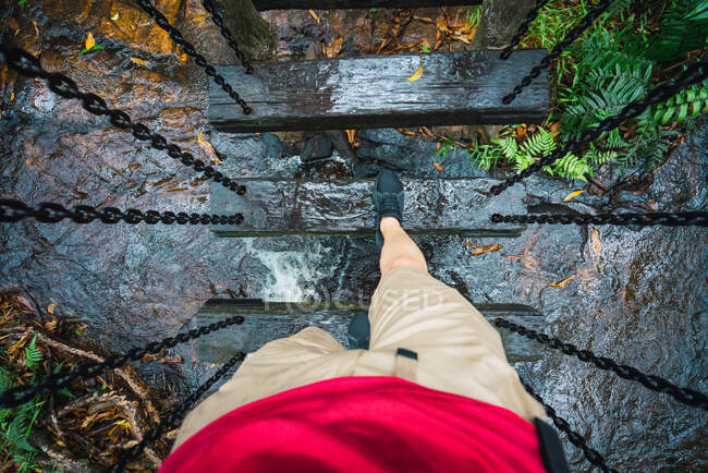 Crop man dall'alto a piedi sul ponte sospeso con travi in legno appeso sopra il flusso del fiume, foresta pluviale di Yanoda — Foto stock