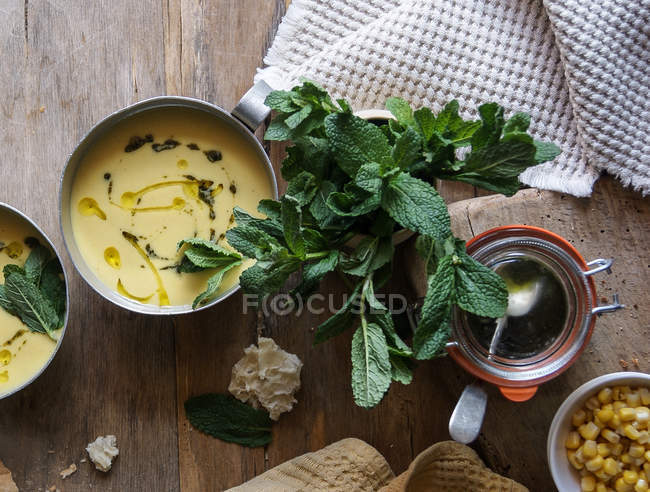 Corn cream soup with coconut and pesto in bowl on wooden table with ingredients — Stock Photo