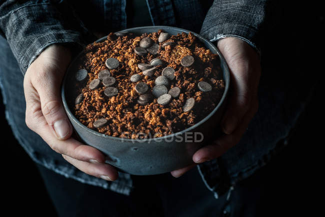 Mãos masculinas segurando tigela de crocante quinoa granola no fundo escuro — Fotografia de Stock
