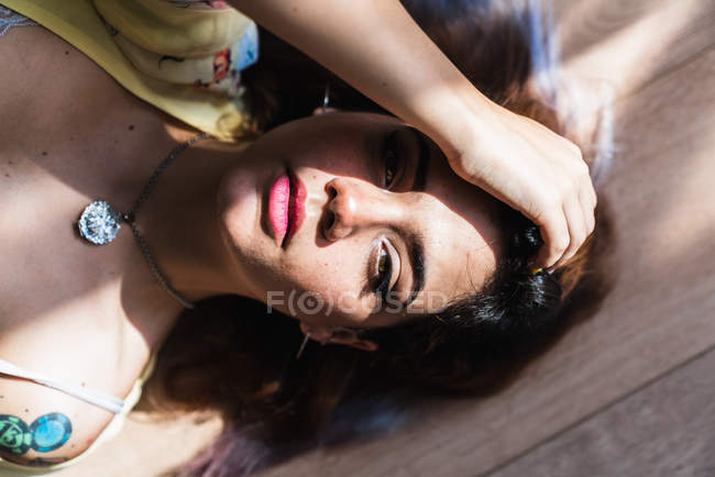 Jovem mulher sedutora olhando para a câmera e tocando o cabelo enquanto deitado no chão — Fotografia de Stock