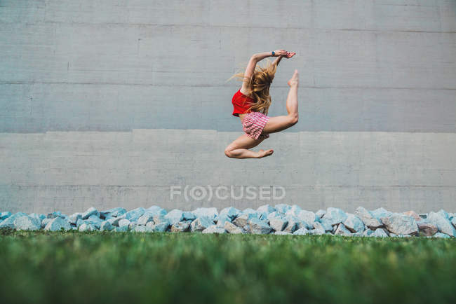 Молодая женщина прыгает высоко в воздухе против кучи камней и бетонной стены — стоковое фото