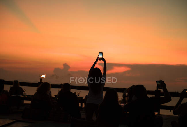 Silhouette di persone che scattano foto con smartphone al mare nelle luci del tramonto in Thailandia. — Foto stock