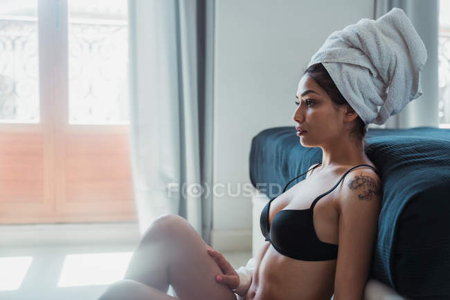 Atractiva mujer reflexiva en lencería y toalla en el pelo sentado en el suelo - foto de stock