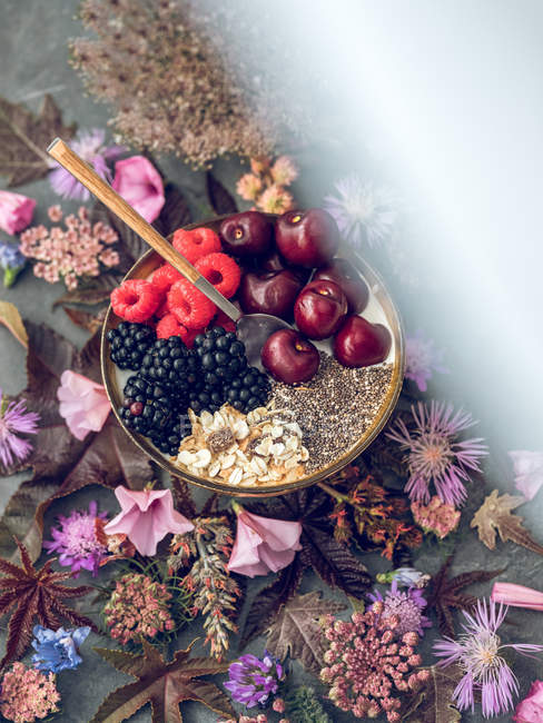 Чиа пудинг с фруктами в миске и винтажной ложкой на столе с цветами и листьями — стоковое фото