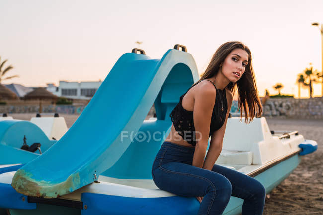 Sensual morena mulher sentada no barco na praia ao pôr do sol — Fotografia de Stock