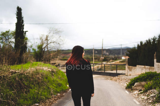 Жінка в чорному з завивки волосся ходіння по дорозі в сільській місцевості — стокове фото