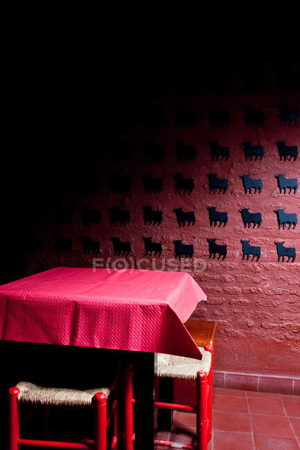 Table recouverte de tissu et chaises placées dans une pièce sombre avec mur en pierre rouge décoré de petits taureaux en papier noir — Photo de stock