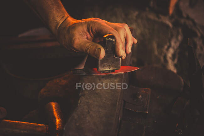 Homem anônimo usando hummer para forjar lâmina de pedaço de metal em oficina profissional — Fotografia de Stock