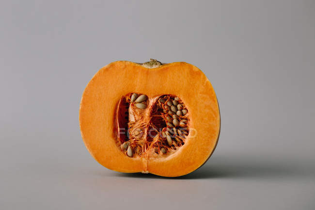 Saftige frische Hälfte des orangefarbenen Kürbisses mit Kernen und Fruchtfleisch auf grauem Hintergrund — Stockfoto