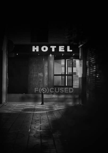 Крыльцо и входная стеклянная дверь с горящей вывеской отеля ночью в черно-белых тонах — стоковое фото