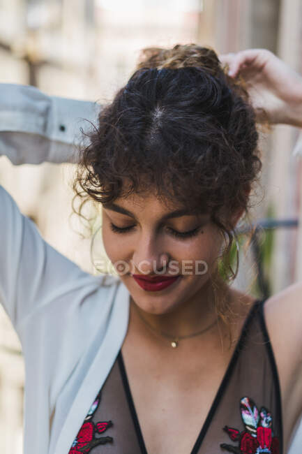 Close-up de encantadora garota encaracolada em brincos e com lábios vermelhos rindo alegremente e olhando para a câmera — Fotografia de Stock