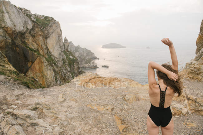 Frau im schwarzen Badeanzug steht am felsigen Ufer — Stockfoto
