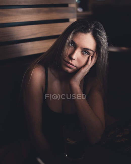 Attractive woman with bright glance in black shirt sitting in wooden room and looking at camera — Stock Photo