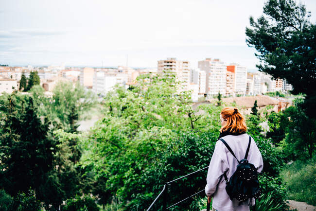 Жінка з сорочкою і рюкзак в повсякденному одязі дивиться місто з лісу — стокове фото
