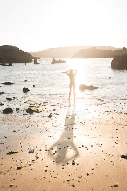 Silhouette of woman standing on wet sand near sea on sunny day — Stock Photo