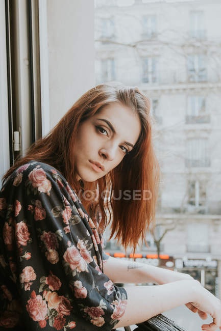 Portrait of Young redheaded woman standing at window — Stock Photo