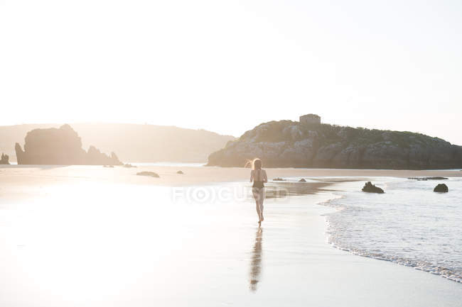 Silhouette de femme debout sur du sable humide près de la mer par une journée ensoleillée — Photo de stock