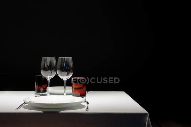 Tabela coberta com pano branco limpo com vidros vazios e placas isoladas em fundo preto — Fotografia de Stock
