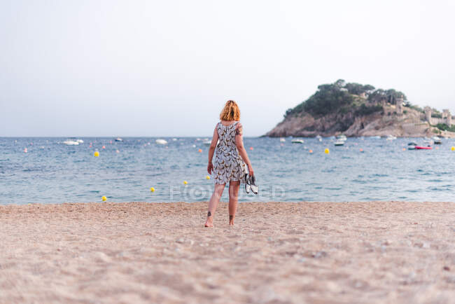 Vue latérale de la culture femme portant des sandales tout en marchant sur la plage de sable fin à l'océan — Photo de stock